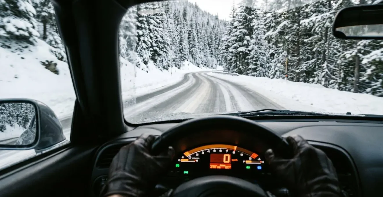 Vue depuis l'habitacle montrant un tableau de bord avec compteur à 30 km/h et route enneigée visible à travers le pare-brise