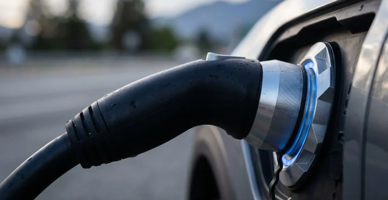 Voiture électrique en charge sur une aire d'autoroute avec famille en pause, paysage de campagne française en arrière-plan